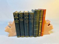 Front view of the full set of antique books with gilded spines standing between the maple leaf marble bookends. Seven books in total with various titles.
