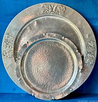 Two round hammered metal serving trays stacked, showing horse silhouette designs on larger tray rim and textured finish on both.