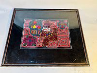 Framed mola tapestry artwork depicting colorful bird and floral designs with geometric stitch patterns under glass.