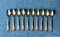 Top view of all 10 silver-plated hammered design teaspoons arranged in a row on blue fabric.