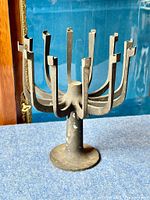 Front and side view of the black metal candle holder showing the twelve arms and round base with visible patina and wear.