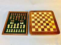 Wooden chessboard alongside inset tray holding complete set of chess pieces laid out in green felt.