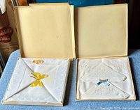 Overview photo showing two open boxes containing Irish linens: one is a pillowcase with lace edges and a yellow ribbon, the other is a set of handkerchiefs with embroidery.