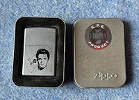 Zippo lighter in a metal case with a portrait of Elvis Presley etched on the front, featuring an E.P.E. (Elvis Presley Enterprises) holographic product sticker on the lid.