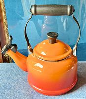 Front view of orange-red gradient enamel Le Creuset kettle with black handle and spout cap