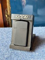Black slim Zippo lighter in plastic display stand with Zippo logo.