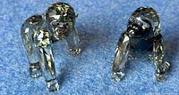 Pair of crystal baby gorilla figurines on blue background, both poses visible