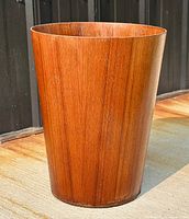 Full view of the circular teak waste basket showing wood grain and shape