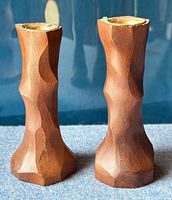 Pair of solid maple wood candlesticks with carved angular brutalist design, standing upright side by side on a flat surface with a blue background.