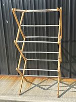 Front view of vintage folding wooden drying rack with multiple horizontal metal rods and wooden frame.