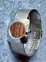 Front angled view of vintage ladies mechanical watch with chrome case and bracelet, showing brown stripe dial and silver hands.