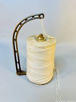 Front and side views of the bronze metal twine holder with beige twine spool, showing the arched holder arm and twine hanging from the top loop.
