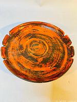 Top view showing swirling black and orange abstract glaze pattern with four cigarette rests on edge.