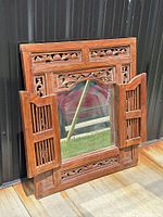 Wall mirror with doors open showing carved teak frame and mirror reflection.