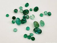 Photo displaying a collection of 24 genuine emerald gemstones of various sizes and cuts on a white background.