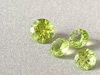 Photo showing four individual round cut lime green peridot gemstones with faceted surfaces reflecting light.