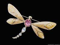 Front view of large vintage butterfly brooch showing pink oval center stone, beige enamel wings, and clear rhinestone tail on black background.