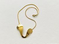 Front wide view of the gold plated Napier pendant necklace laid flat showing the delicate chain and sculptural abstract pendant.