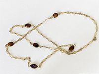 Full view of the gold-tone necklace laid flat on a white background showing oval brown stones and decorative chain links.