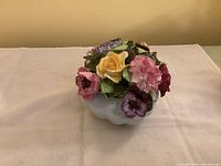 Porcelain flower basket figurine with detailed multi-colored flowers and white basket base on a cloth background
