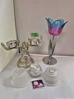Metal two-arm deer head candle holder, metal candle holder with pink/blue glass flower shade, two frosted glass candle shades, and clear glass candle holder arranged on white surface