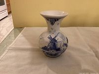 Front side of the vase showing blue windmill and landscape design on white ceramic.