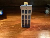 Front view of blue and white ceramic Delft house with six rows of windows and a base door, yellow chimney on roof.