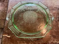 Top-down photo of green footed cake plate with visible etched floral center and geometric patterned border, two handles at opposite sides.