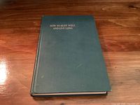 Green hardcover book with gold embossed title on front cover, placed on wooden surface.