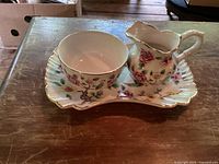Set including creamer, sugar bowl, and tray on wooden table, showing floral pattern and gold trim.