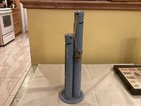 Photo of blue Looney Tunes coin bank with three vertical cylindrical tubes for coin insertion, one with a chain and Looney Tunes charm, on a round base.