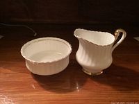Photo of cream pitcher and sugar bowl with gold trim on a wood surface