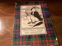 Photo of the front cover of the book 'Mair Canny Tales Fae Aberdeen'. The cover shows traditional tartan pattern and vintage illustration of children.