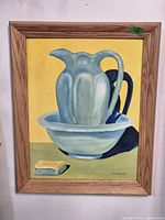 Front view of the oil painting 'Jug' by D.E. Mahoney showing the jug and bowl with a small object on the table, framed in wood.