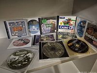 Photo shows 10 PC game discs and cases arranged on surface. Titles include casino and various game genres.