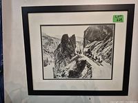 Framed black and white picture of a wagon and horses on a mountain path with rock formations