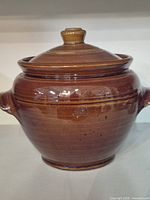 Front view of brown pottery pot with lid showing rounded shape and gloss finish.