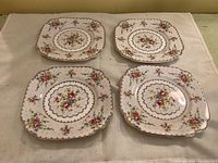 Four square floral dessert plates with scalloped edges and gold trim, showing the front design.