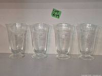 Front view of 4 vintage etched juice glasses standing upright, showing floral etching details and round footed bases.