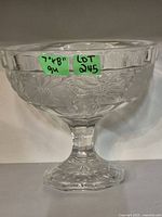 Front view of clear pressed glass pedestal bowl with floral pattern, showing scalloped rim and embossed flower design.