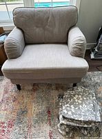 Grey fabric armchair against window, showing cushioned arms and wooden legs with folded floral patterned additional cover beside it.