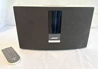 Front view of the Bose SoundTouch 20 speaker with remote placed beside it on a white surface.