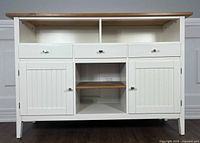 Front view of white-painted wooden buffet sideboard with three drawers, two cabinet doors and central open shelving