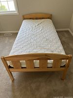 Bottom twin bed frame with newer mattress and white quilted topper, showing wood headboard and footboard with vertical slats.