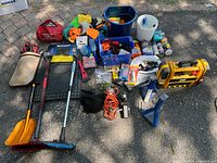 Overview of assorted car maintenance and emergency items laid on ground including CAT Juno starter, booster cables, cleaning supplies, snow scrapers, floor mats, and organizing bins.