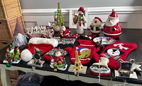 Full lot overview on black table showing tree skirt, multiple stockings with colorful designs, Santa hat, various Santa and snowman ornaments, green tree ornament, and metal rocking horse stocking holders.