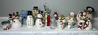 Wide view showing full lot of Christmas snowman collectibles including mugs, figurines, candle holders, and decorative items arranged on table