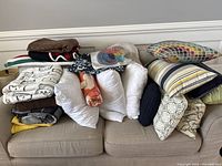 Wide view of couch covered with various folded blankets and stacked decorative pillows