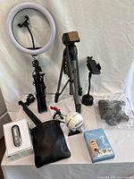 Full lot view showing ring light with tripod, Optex T165 tripod, Blue Snowball ICE microphone, Magshot phone holder, accessories, and headphones on table.