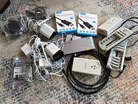 Full lot showing security cameras, battery chargers with AA batteries, powerline adapters, USB cables and USB port device on carpet